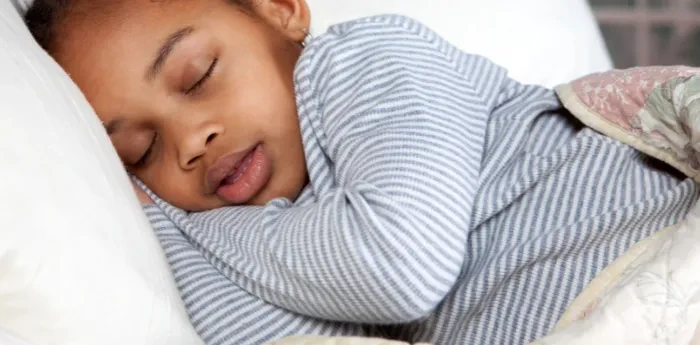 Young child peacefully sleeping on their side in bed, wearing striped pajamas and covered with a blanket.