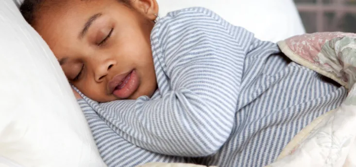 Young child peacefully sleeping on their side in bed, wearing striped pajamas and covered with a blanket.