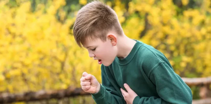 Young boy coughing outdoors in front of yellow foliage, illustrating potential pediatric airway issues.