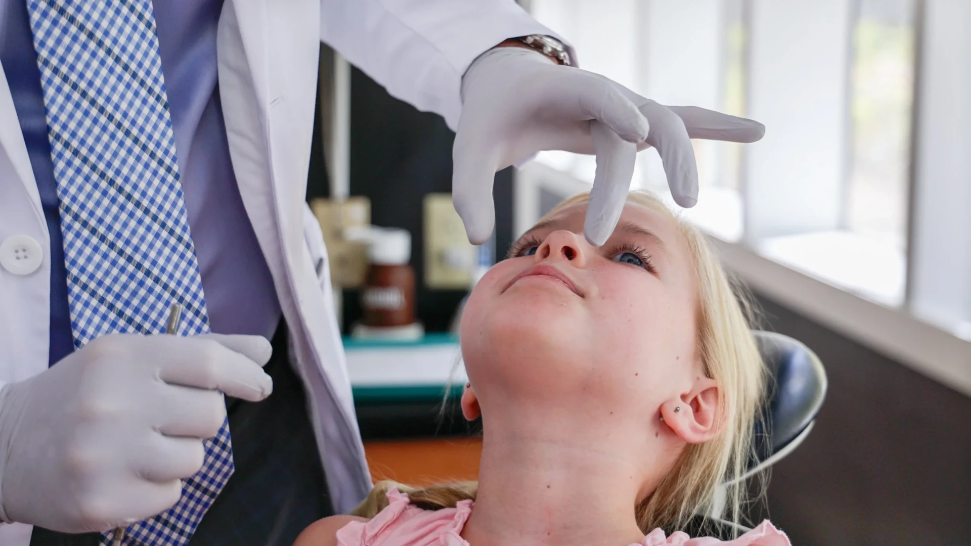 Dentist in gloves examining a young girl’s airway and nasal area while she reclines in a dental chair.