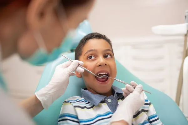 Smiling boy sitting in a dental chair while the dentist examines his teeth with dental tools.