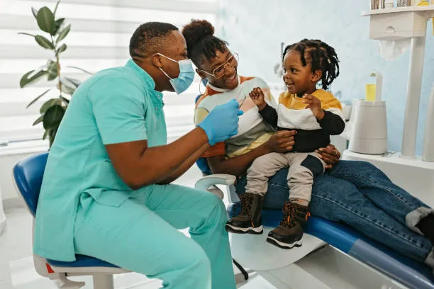 Dentist interacting playfully with a toddler on their parent’s lap during a pediatric dental visit.