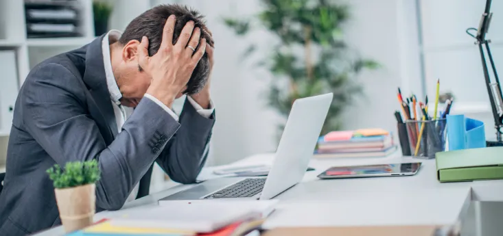 Stressed man at a desk with a laptop and paperwork, representing breathing and focus challenges linked to sleep and airway health.