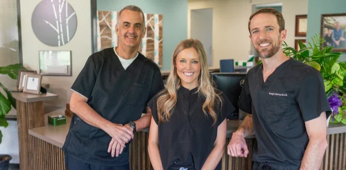 Dental Goals for the New Year – three dentists standing and smiling at the front desk of Atkins & Anderson DDS office.