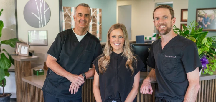 Dental Goals for the New Year – three dentists standing and smiling at the front desk of Atkins & Anderson DDS office.
