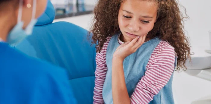 Child holding her cheek in pain from winter tooth sensitivity, showing a common cause of tooth sensitivity in cold weather.