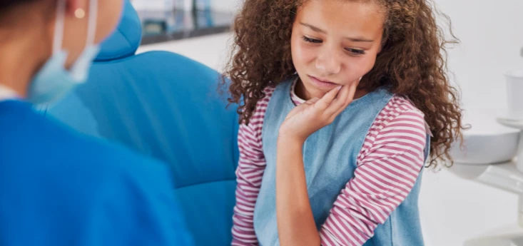 Child holding her cheek in pain from winter tooth sensitivity, showing a common cause of tooth sensitivity in cold weather.