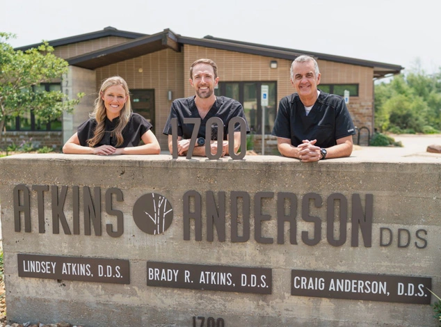 Our dentist at atkins and anderson standing behing our dentist office sign