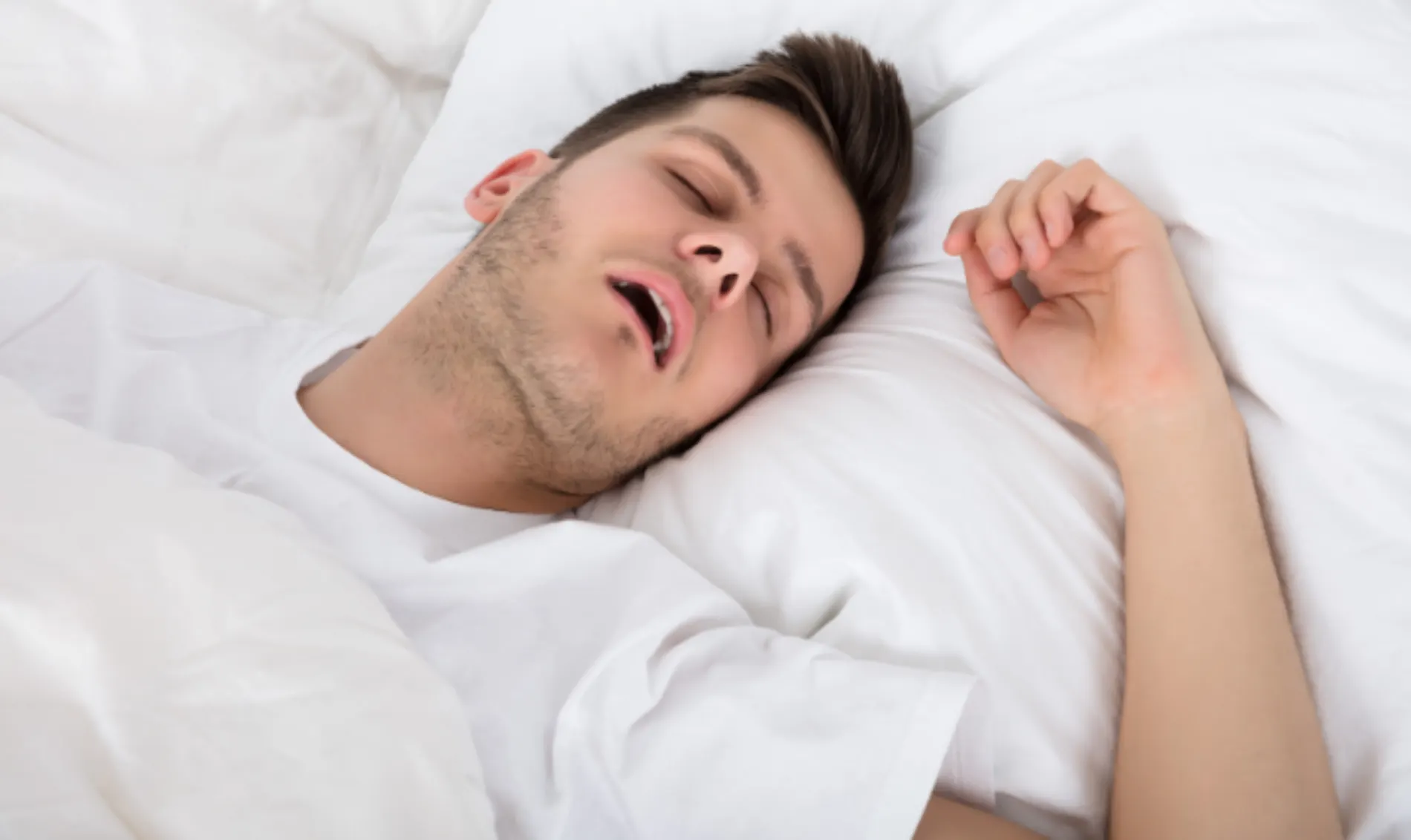 Why Do I Snore? Snoring & Sleep Apnea. Man in white t-shirt snoring in on back on white bed.